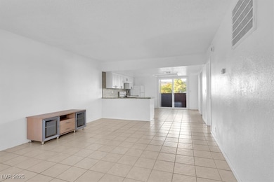 Unfurnished living room featuring light tile patterned flooring, a textured wall, and a textured ceiling