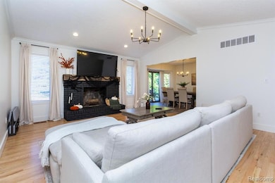 Living room with light wood-style flooring, a brick fireplace, ornamental molding, recessed lighting, and a chandelier