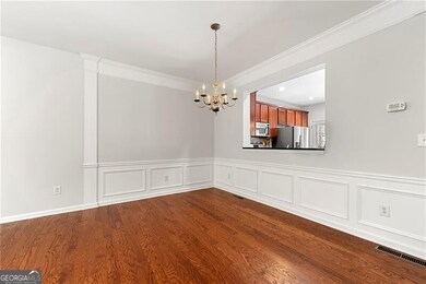 Dining area with a chandelier, dark wood finished floors, a wainscoted wall, ornamental molding, and a decorative wall