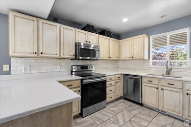 Kitchen with light brown cabinetry, appliances with stainless steel finishes, decorative backsplash, light stone countertops, and recessed lighting