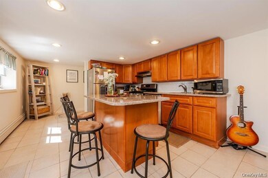 Kitchen featuring light stone countertops, tasteful backsplash, brown cabinetry, appliances with stainless steel finishes, and a kitchen breakfast bar