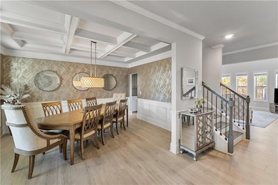 Dining space featuring stairs, light wood-style flooring, a wainscoted wall, beamed ceiling, and coffered ceiling
