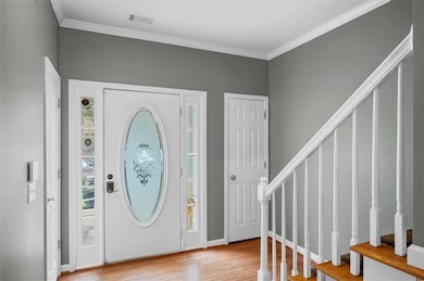 Foyer entrance featuring ornamental molding, light wood-type flooring, and stairs