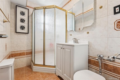 Bathroom with tile walls, toilet, a shower stall, vanity, and tile patterned floors