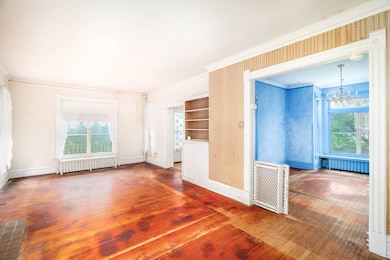 Empty room with wallpapered walls, hardwood / wood-style floors, radiator heating unit, crown molding, and a chandelier
