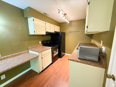 Kitchen with black appliances, light wood finished floors, white cabinets, rail lighting, and under cabinet range hood