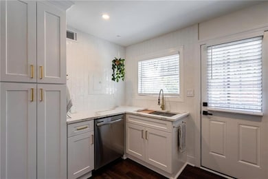 Kitchen featuring stainless steel dishwasher, a sink, dark wood-style floors, white cabinetry, and light stone counters