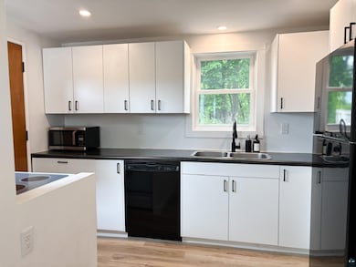 Kitchen featuring black dishwasher, stainless steel microwave, dark countertops, freestanding refrigerator, and recessed lighting