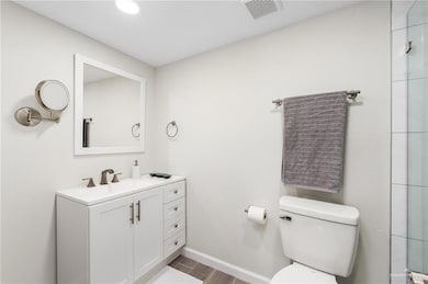 Full bathroom with wood finished floors, visible vents, toilet, vanity, and baseboards