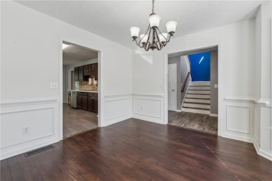 Dining room with a chandelier, dark wood-style flooring, wainscoting, a decorative wall, and stairs
