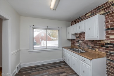 Kitchen featuring dark countertops, white cabinetry, dark wood-style flooring, and brick wall