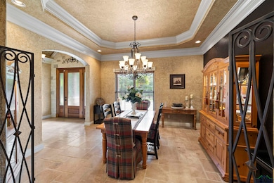 Dining area with stone tile flooring, a tray ceiling, ornamental molding, arched walkways, and a chandelier