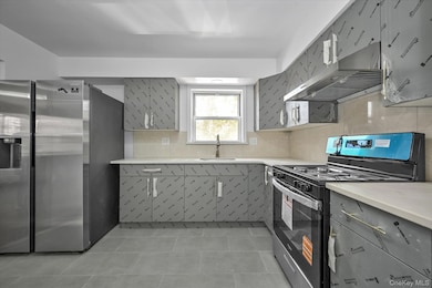 Kitchen featuring appliances with stainless steel finishes, tasteful backsplash, under cabinet range hood, gray cabinets, and light tile patterned floors