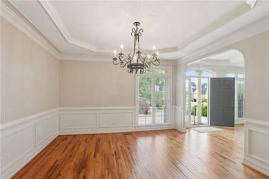 Foyer featuring arched walkways, a raised ceiling, light wood-style floors, a decorative wall, and crown molding
