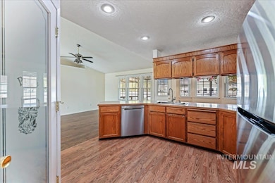 Kitchen with stainless steel appliances, brown cabinetry, light wood-style flooring, vaulted ceiling, and a textured ceiling