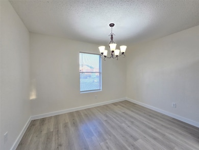 Empty room featuring light wood finished floors, a textured ceiling, and a chandelier