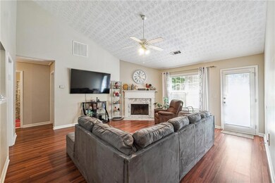 Living room with dark wood-style floors, a ceiling fan, a stone fireplace, and high vaulted ceiling