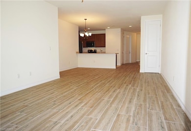 Unfurnished living room featuring a chandelier, light wood finished floors, baseboards, and recessed lighting