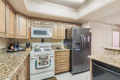 Kitchen with white appliances, light stone countertops, and light tile patterned floors