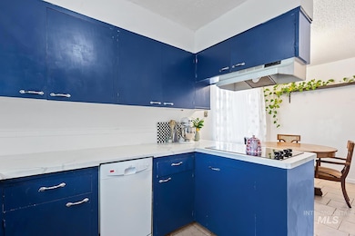 Kitchen with blue cabinetry, a peninsula, white dishwasher, light tile patterned floors, and a textured ceiling