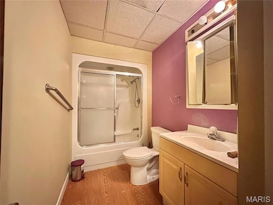 Full bathroom with a drop ceiling, light wood finished floors, vanity, and shower / bath combination with glass door