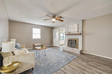 Living area with a ceiling fan, a textured ceiling, wood finished floors, baseboards, and a brick fireplace