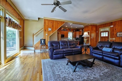 Living room featuring ornamental molding, wood walls, light wood-type flooring, ceiling fan, and stairway