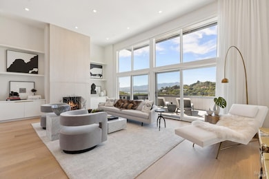 Dramatic living room with soaring ceilings, floor to ceiling windows, limestone fireplace and views of the bay and Mt Tam.
