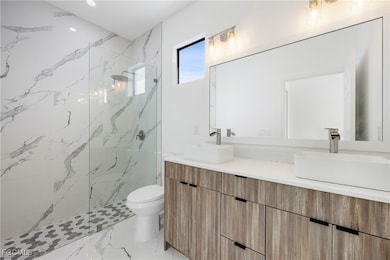 Full bathroom with double vanity, a marble finish shower, and light marble finish floors