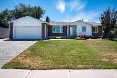 Ranch-style home with decorative driveway, an attached garage, a chimney, a front yard, and brick siding