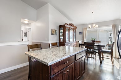 Kitchen with dark brown cabinets, a kitchen island, vaulted ceiling, pendant lighting, and a chandelier