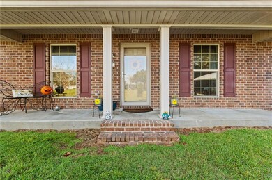 Doorway to property featuring covered porch, brick siding, and a yard