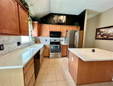 Kitchen with black appliances, backsplash, light tile patterned floors, brown cabinetry, and light stone countertops