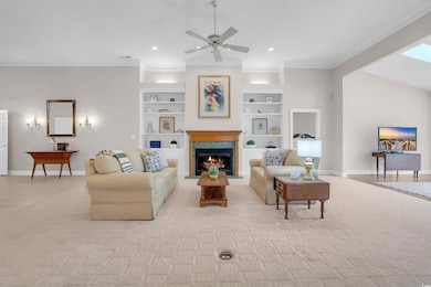 Living area with crown molding, a ceiling fan, a lit fireplace, built in features, and recessed lighting