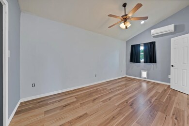 Unfurnished bedroom with vaulted ceiling, light wood-type flooring, a ceiling fan, and a wall mounted air conditioner