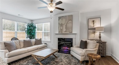 Living area with baseboards, dark wood finished floors, a ceiling fan, and a warm lit fireplace
