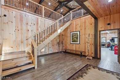 Stairs featuring a towering ceiling, wooden walls, wood finished floors, a wood ceiling with exposed beams, and recessed lighting