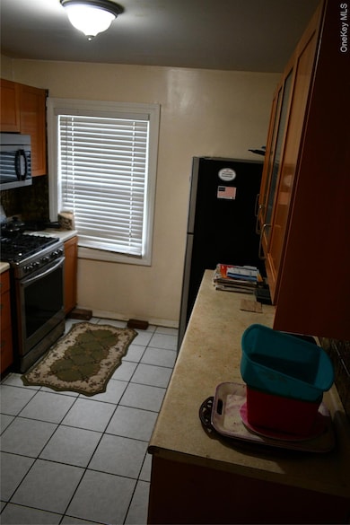 Kitchen featuring light tile patterned floors, stove, brown cabinets, light countertops, and freestanding refrigerator
