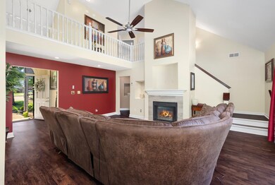 Living area featuring wood finished floors, high vaulted ceiling, a tiled fireplace, a ceiling fan, and baseboards