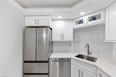 Kitchen featuring stainless steel appliances, tasteful backsplash, white cabinetry, light countertops, and glass insert cabinets
