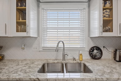 Kitchen featuring glass insert cabinets, decorative backsplash, and white cabinetry