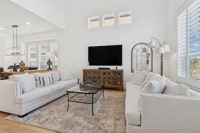 Living area featuring wood finished floors, healthy amount of natural light, a chandelier, a high ceiling, and recessed lighting