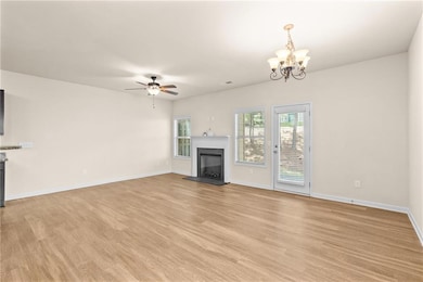Unfurnished living room featuring light wood finished floors, a fireplace with raised hearth, a ceiling fan, and a chandelier