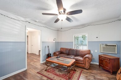 Living room with a textured ceiling, wood finished floors, wainscoting, ceiling fan, and crown molding