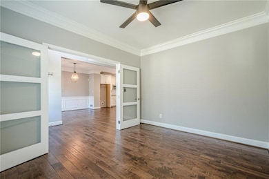 Spare room featuring ornamental molding, ceiling fan, dark wood-style floors, a chandelier, and a wainscoted wall