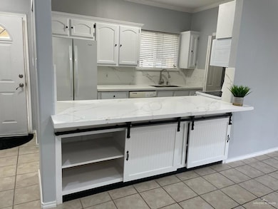 Kitchen with white cabinets, freestanding refrigerator, light tile patterned flooring, light stone countertops, and ornamental molding