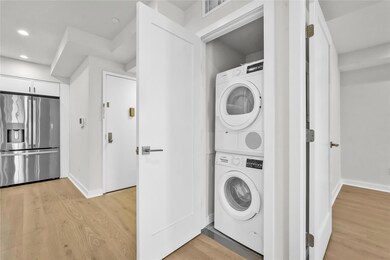 Laundry room featuring stacked washing machine and dryer, light wood-style floors, baseboards, and recessed lighting