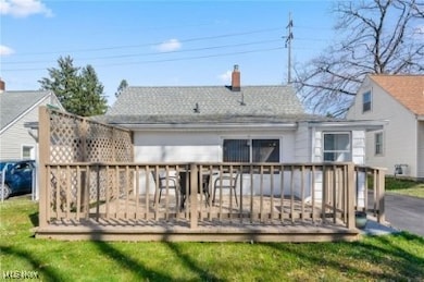 Rear view of property featuring a wooden deck, a chimney, roof with shingles, and a yard