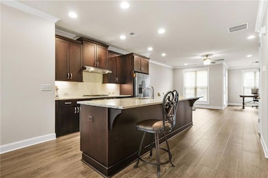 Kitchen featuring a breakfast bar area, dark brown cabinets, an island with sink, decorative backsplash, and ornamental molding