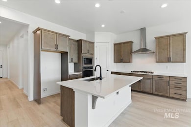 Kitchen with wall chimney exhaust hood, stainless steel appliances, light wood finished floors, decorative backsplash, and recessed lighting